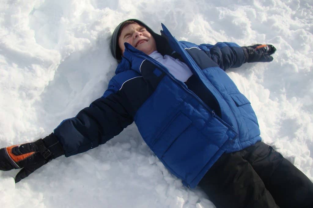 child in blue ski jacket making a snow angel