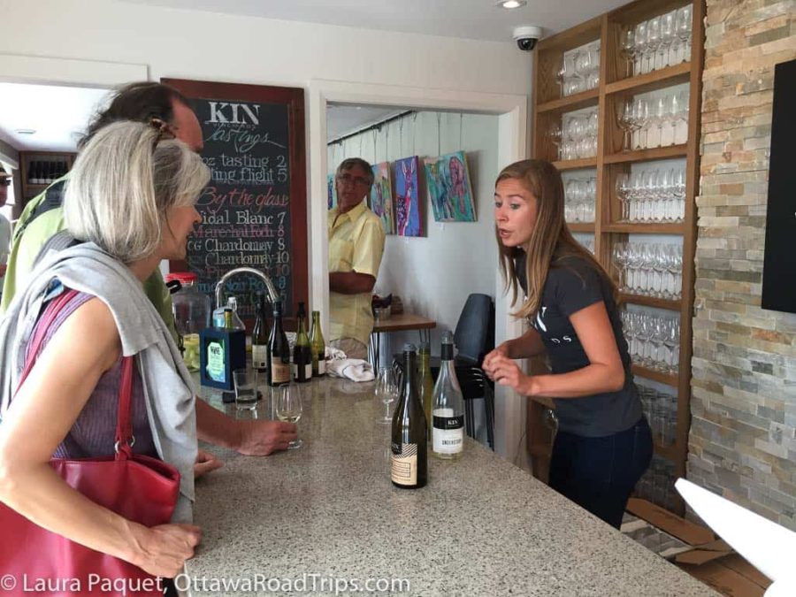 Young woman serving wine to customers at long counter at KIN Vineyards in Carp, Ontario.