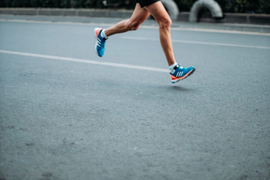bare legs with blue sneakers running along the pavement