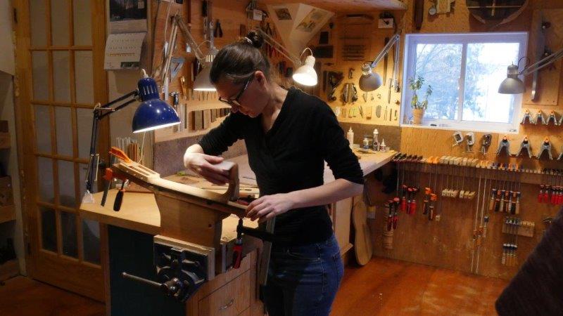 young woman in black clothes sanding and building a wooden guitar in a workshop