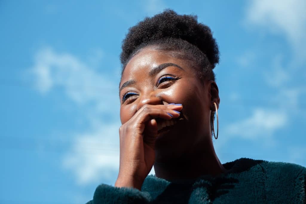 woman covering her mouth and laughing against backdrop of blue sky