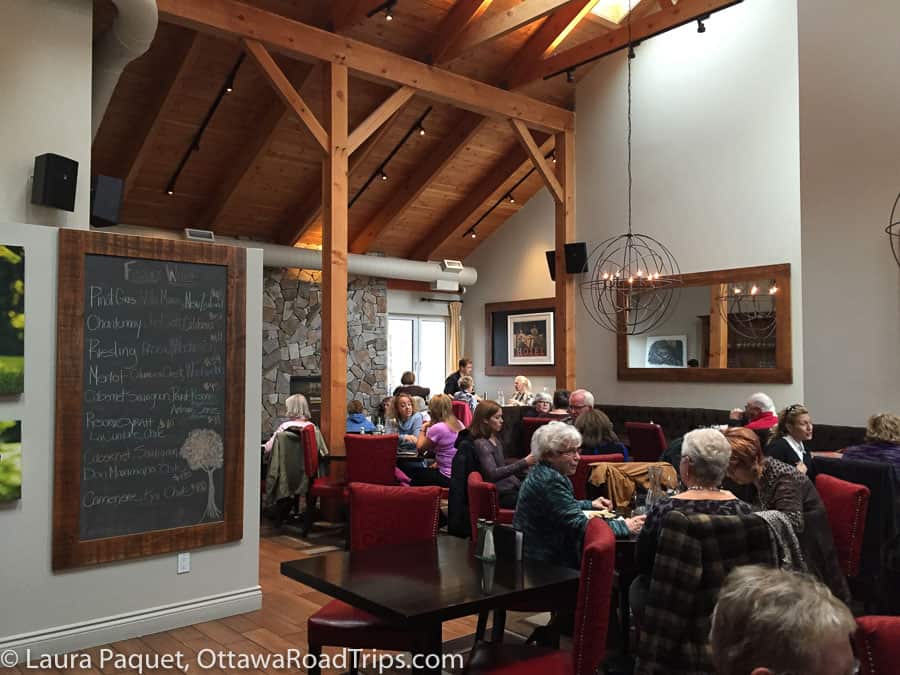 restaurant room with stone wall, sloping wood ceiling, rustic-modern pendant lamps, wine list on large chalkboard at black dog bistro in manotick.