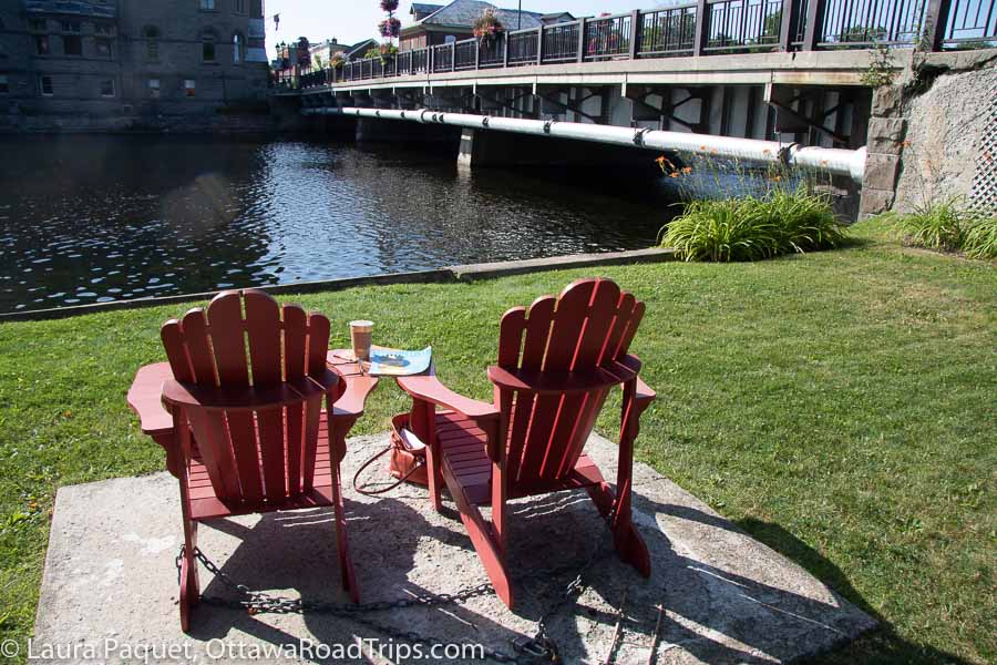 two red chairs on a patio beside the mississippi river and the bridge in carleton place, ontario.