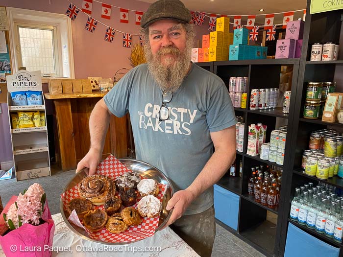 bearded man in crusty bakers t-shirt holding a silver tray of pastries