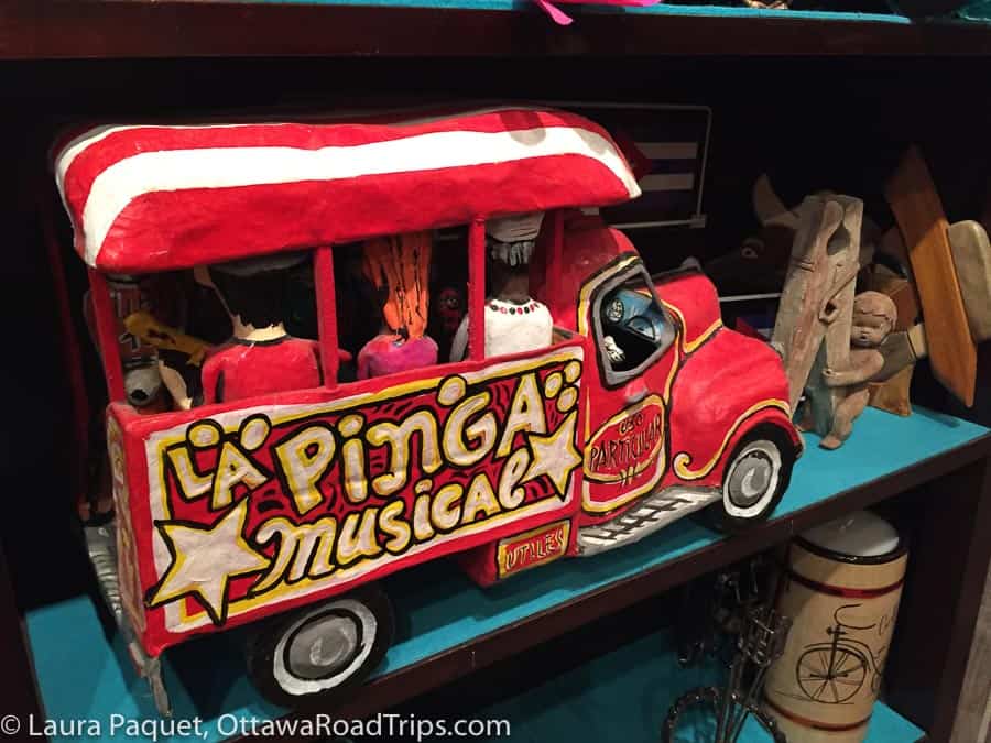 red-and-yellow papier maché mini-bus toy on shelf with wooden items at one world bazaar in manotick, ontario.