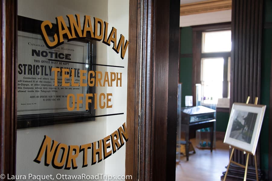 glass door with gold letters reading "canadian northern telegraph office" opening onto old green office with wooden trim in background.