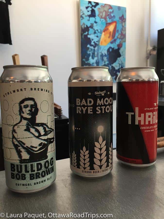 three beer tins on a counter with a blue-and-yellow painting in the background