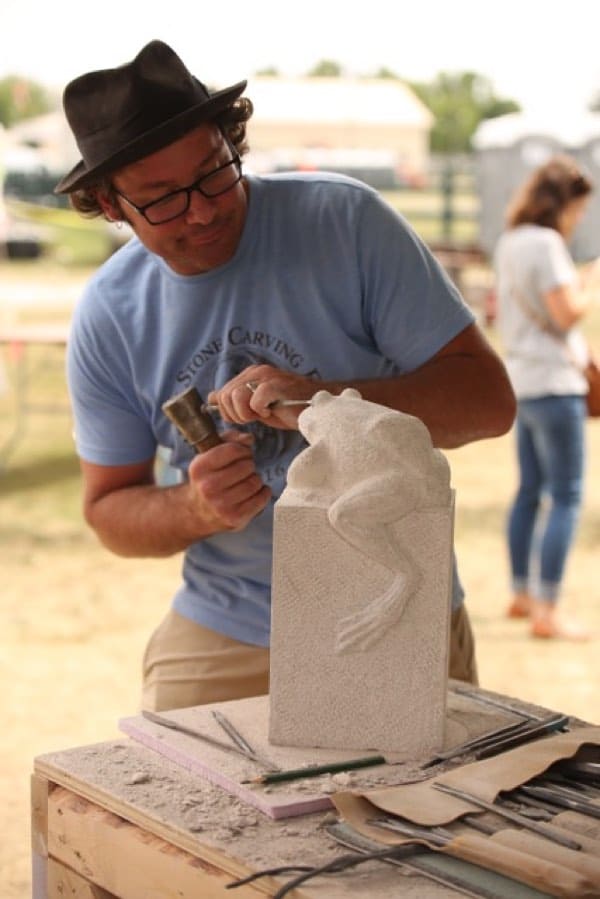 Man in blue t-shirt carving a white piece of stone with a chisel