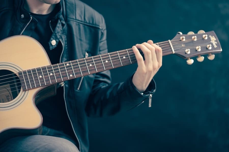 close up of someone's hands on the neck of an acoustic guitar, playing a chord