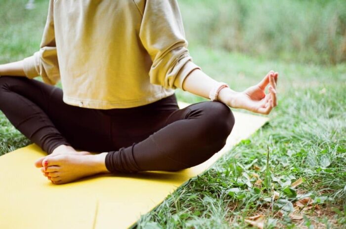 torso and legs of a woman meditating on a yoga mat on a green lawn