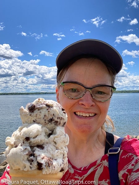 woman with blue baseball cap holding ice cream cone with river in background