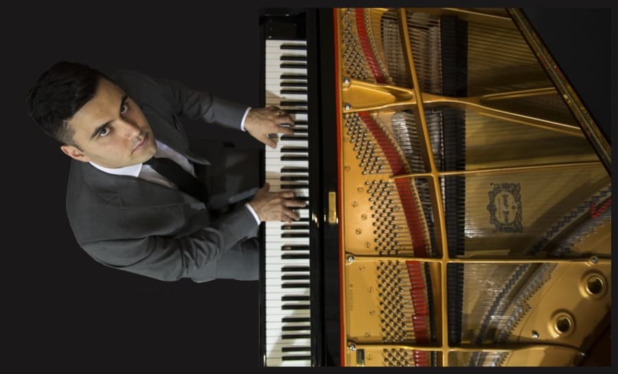 photo of man in suit playing an open piano, taken from above