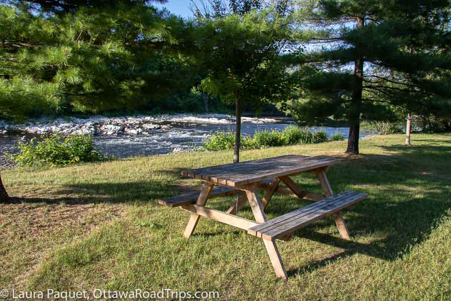 empty wooden picnic table with conifers and river rapids in background