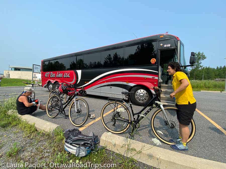 red and black bus in parking lot with five bikes and two cyclists in foreground