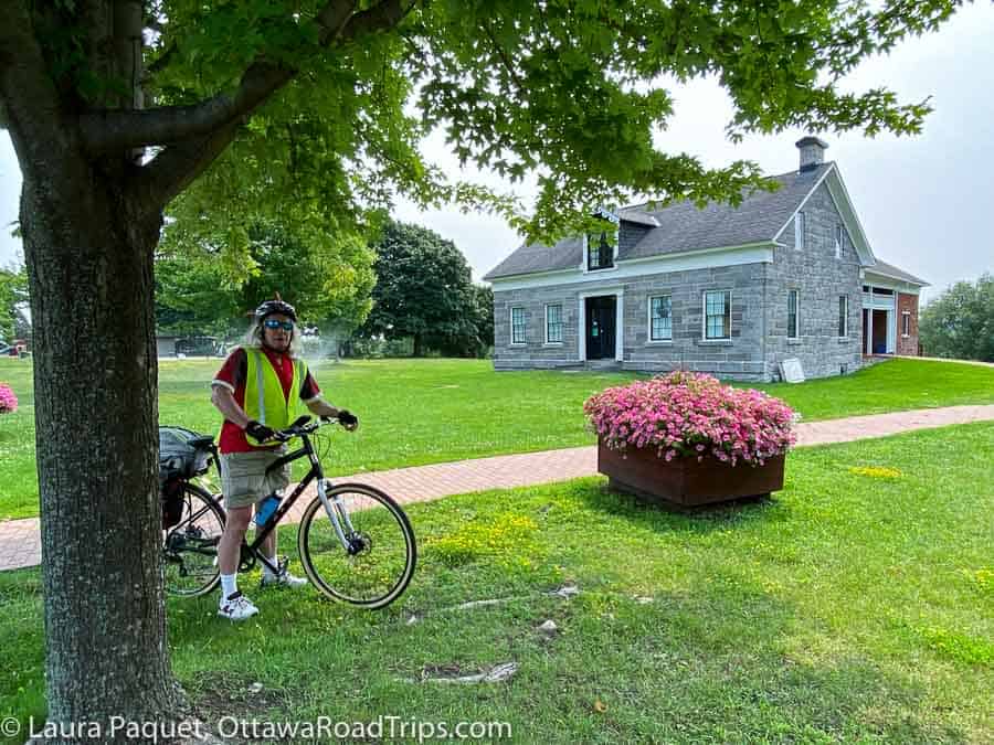 man on bike under tree in front of old stone house (cornwall community museum and archives)