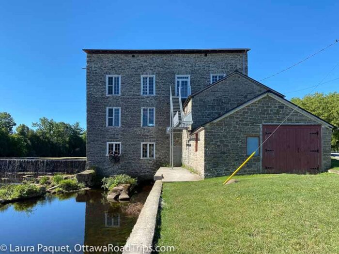 grey stone three storey mill next to a watercourse