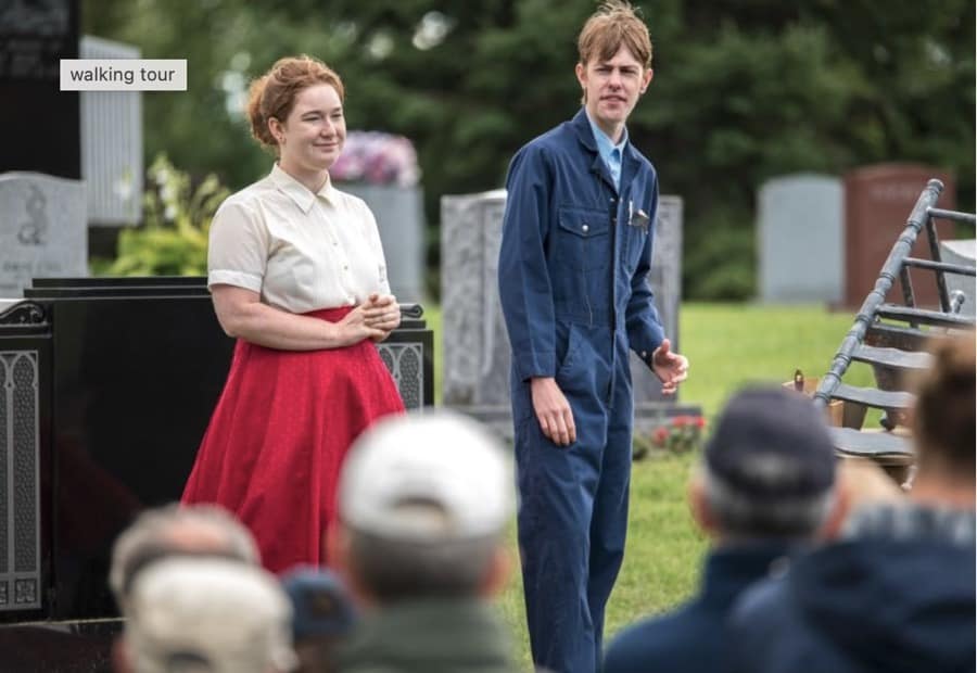 A woman and a man in 1940s clothes on an outdoor stage, with audience members in the foreground.