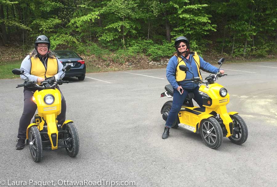 Two women on yellow e-scooters in a parking lot