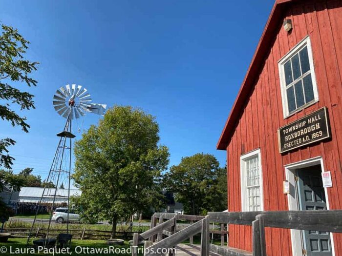 glengarry-pioneer-museum-dunvegan - Ottawa Road Trips two-storey building with reddish siding, with a split-rail fence in foreground and windmill in background