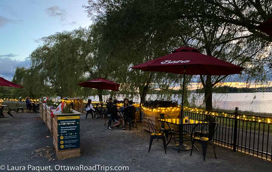restaurant patio with burgundy umbrellas and fairy lights with sunset and river in background