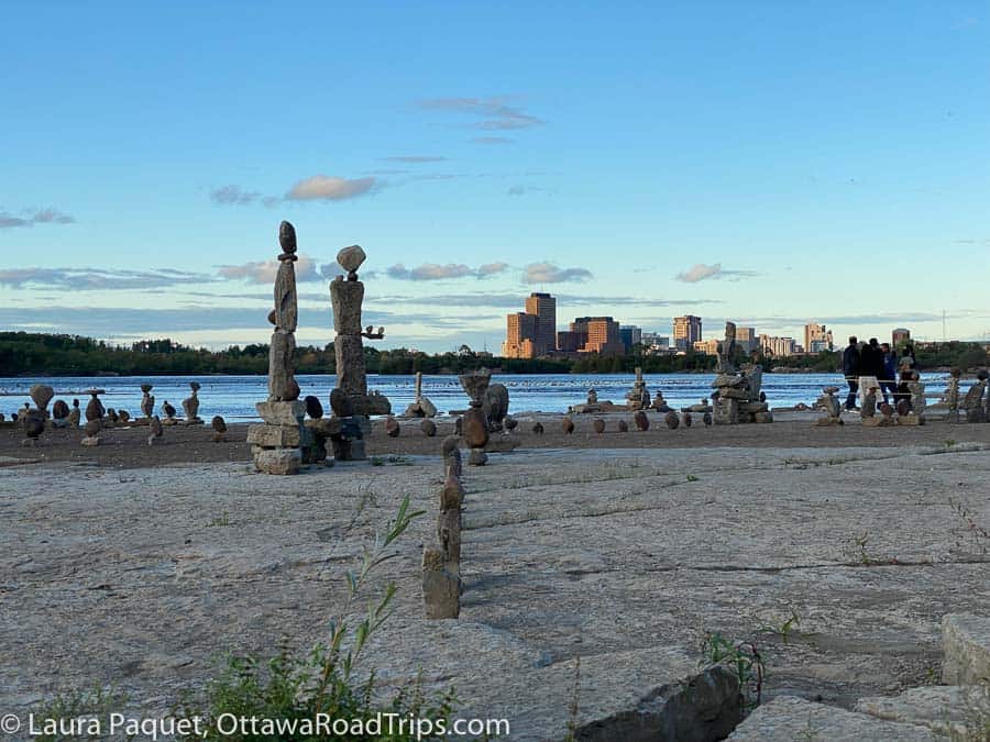 grey river rocks arranged along a flat rock shoreline in dozens of sculptures of various heights