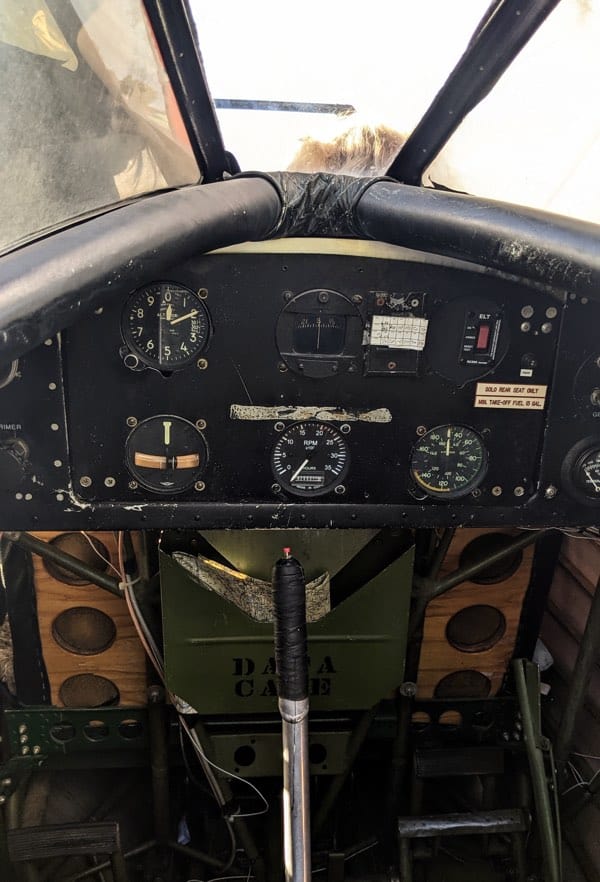black and wooden dashboard of instrument panel in 1939 waco upf-7 biplane, with passenger seated in front of the windshield.