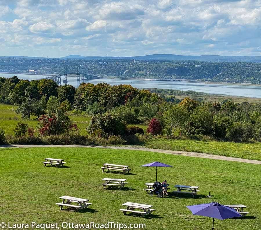 picnic tables with blue umbrellas on a green lawn overlooking the st. lawrence river and the ile d'Orleans bridge
