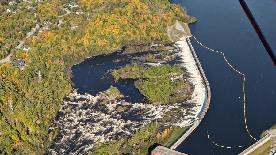 aerial view of farmer's Rapids generating station on the Gatineau River, framed by trees just starting to show fall colours.