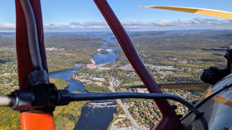 aerial view of gatineau river with rapids and power stations, framed by fuselage and wings of a biplane.