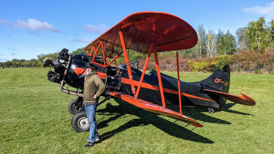 man in baseball cap, brown jacket and jeans in front of 1939 waco upf-7 black-and-red biplane at rockcliffe airport in ottawa.