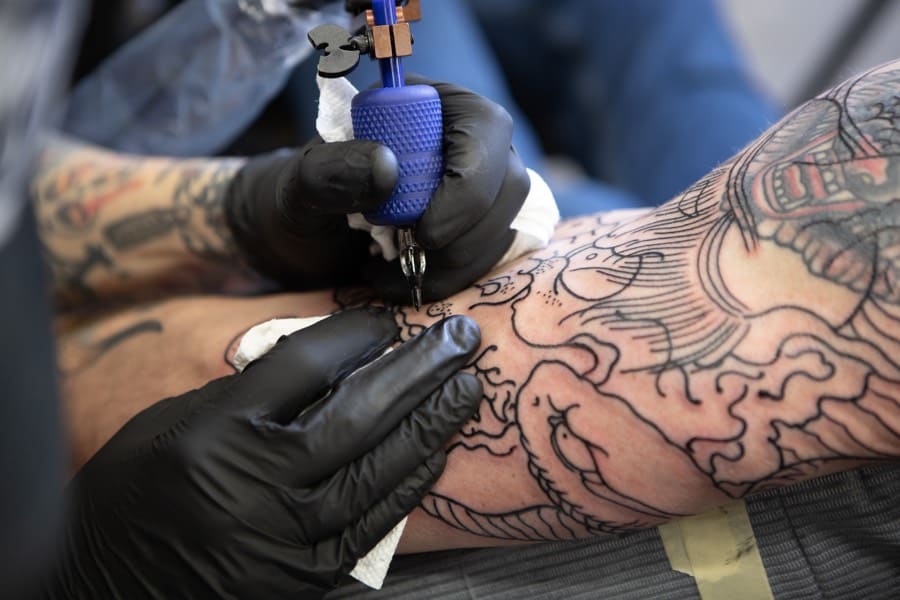 Close-up of tattoo artist's hands creating black line outlines of tattoos on an arm.