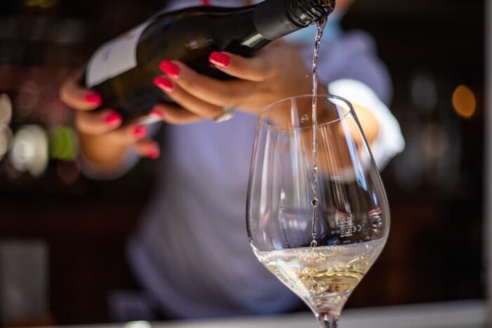 woman's hands holding a bottle pouring white wine into a glass