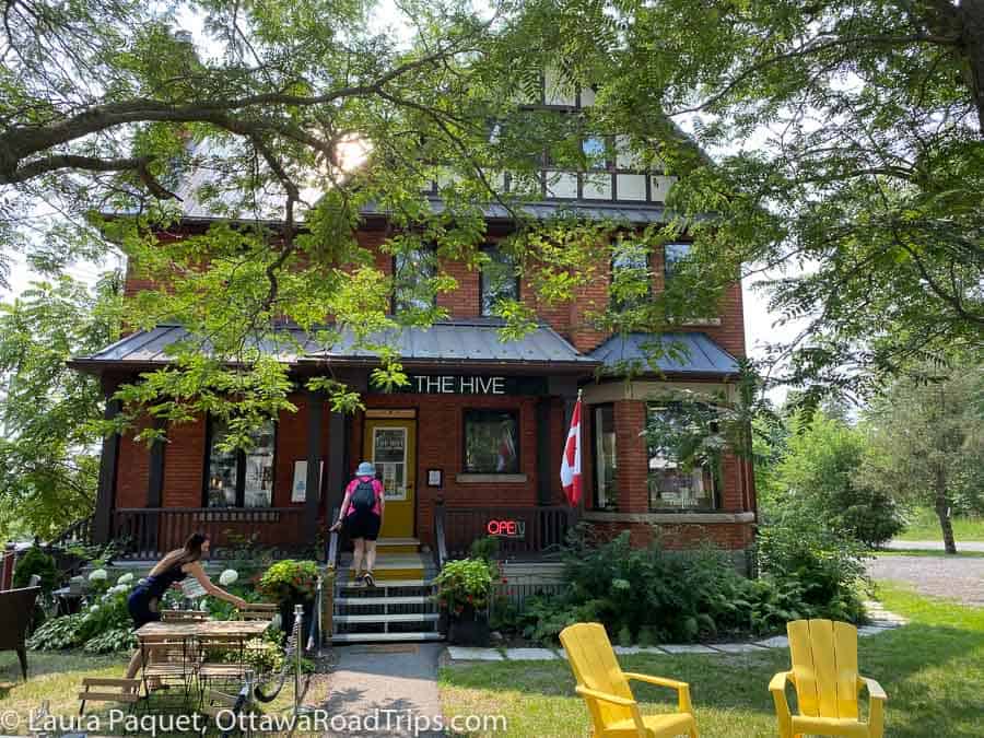 red-brick, three-storey house with large porch and yellow muskoka chairs out front.