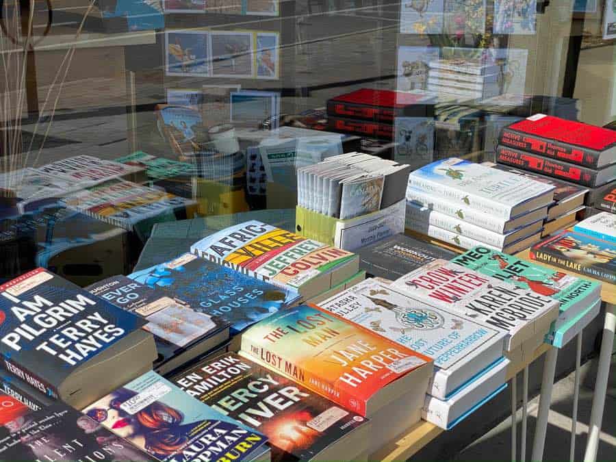 hardcover books displayed on a table, in a window with reflections of the street.