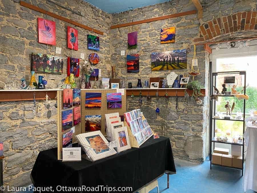 small paintings displayed on an old stone wall, with vases, ornaments and gift cards displayed in foreground, at the priest's Mill Arts Centre.