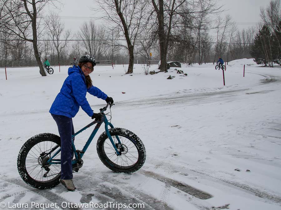 woman in a blue coat on a fat bike in a snowy parking lot