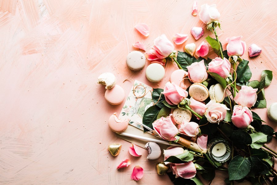 Pink roses and pink and white macarons on a pale pink background.