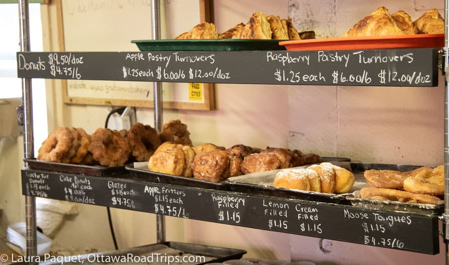 metal shelves of fritters, doughnuts and other baked goods, with chalked prices below them.