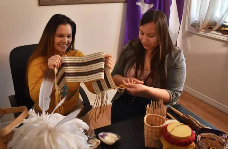 two young Mohawk women sitting at a table holding a Wampum belt