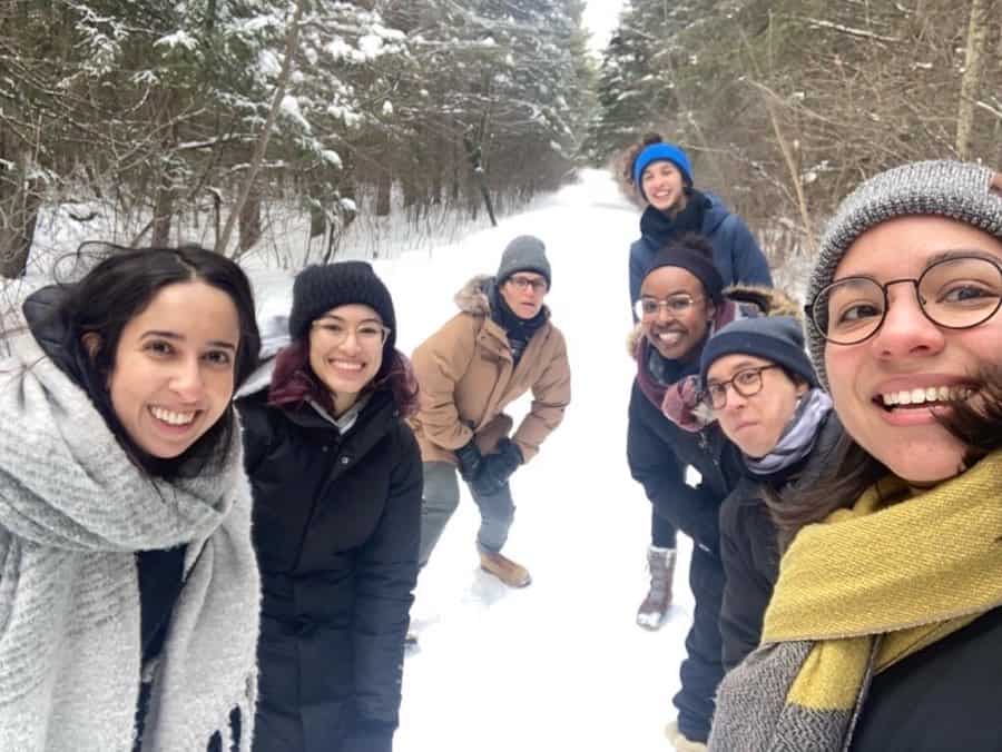 A group of young BIPOC hikers in parkas and toques smiling on a snowy hiking trail.