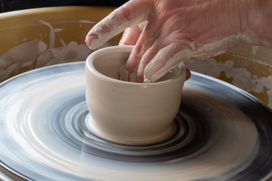 closeup of two hands spinning a small bisque-coloured bowl on a pottery wheel