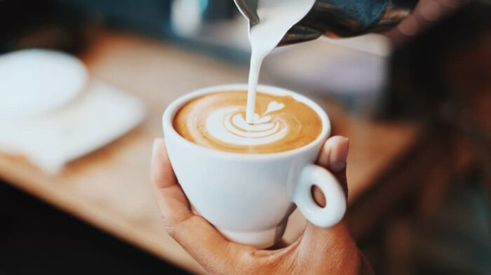 closeup of someone pouring cream into a small white cup of coffee