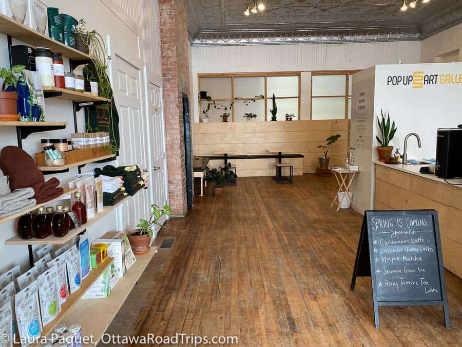 fifth chute coffee in eganville with wooden floors, pressed tin ceilings, chalk sandwich board, and floating shelves stocked with toques, tea and maple syrup.