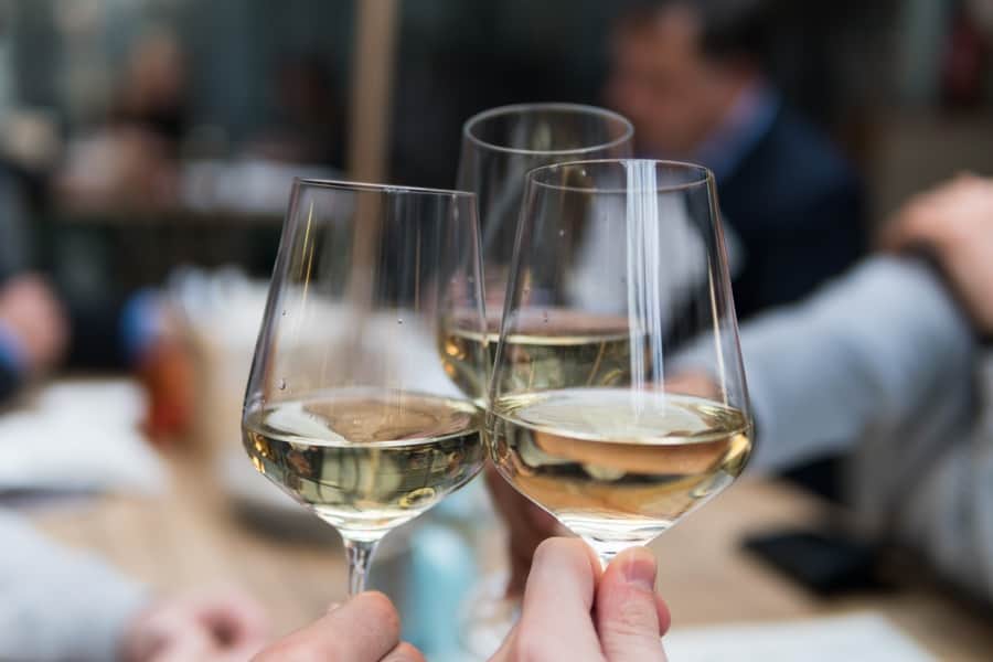 three glasses of white wine being clinked against a blurred background