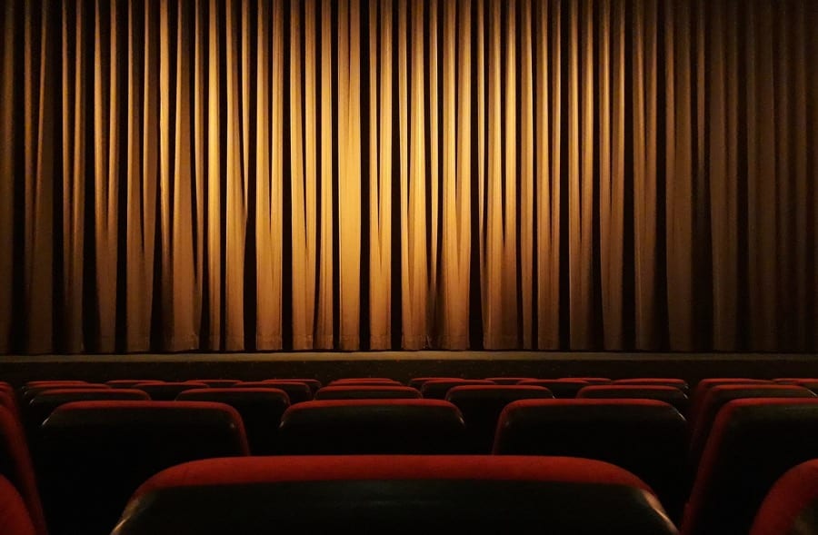 The backs of red seats in an empty theatre, facing a gold curtain. Image by Andreas Glöckner from Pixabay 