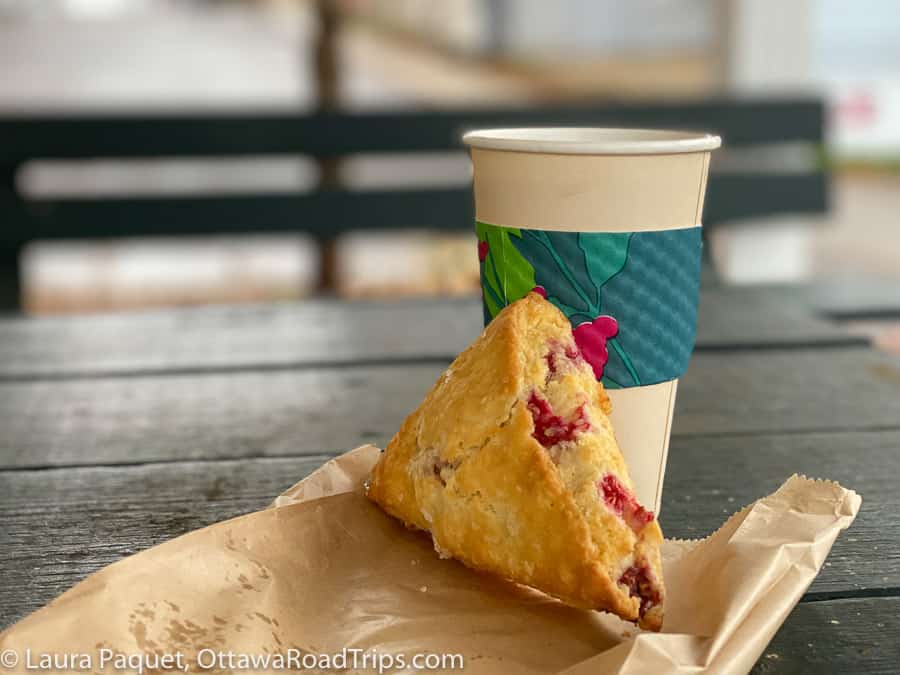 closeup of a raspberry scone on a paper bag, with a paper cup of tea in the background, from vanilla beans cafe and creamery in westport, ontario.