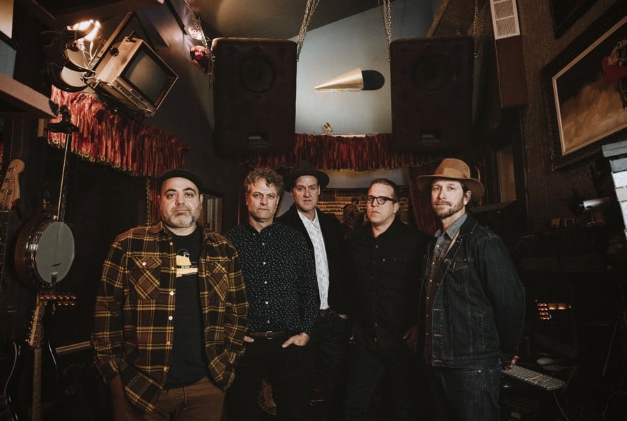 five men standing in front of a stage, and a banjo and other musical instruments