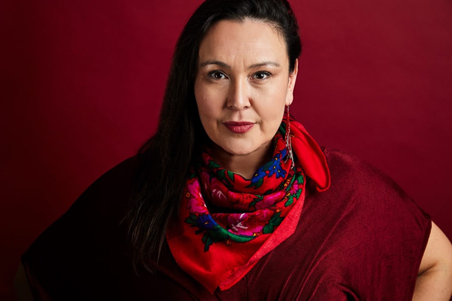 Dene woman in a red top with a red patterned scarf against a red background.