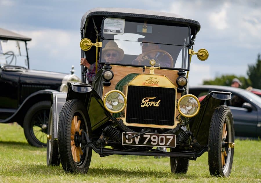 A man and woman inside a Ford Model-T parked on grass.