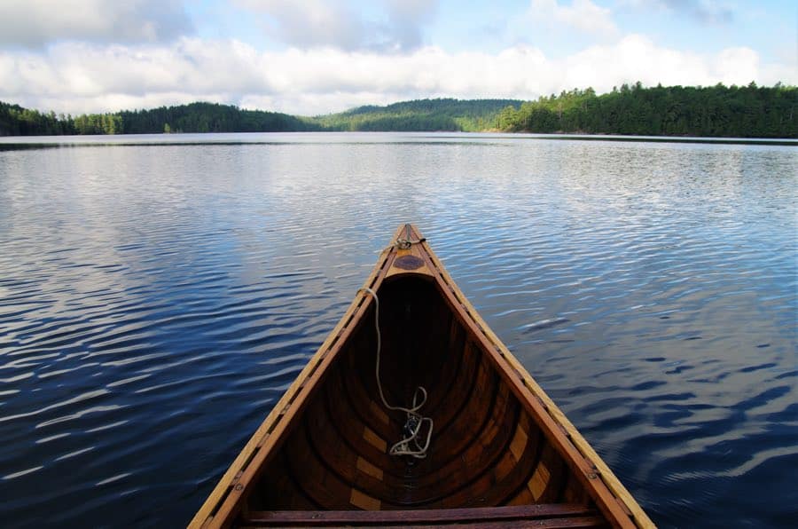 view of the bow of a wooden canoe, with flat water and low wooded hills in  background